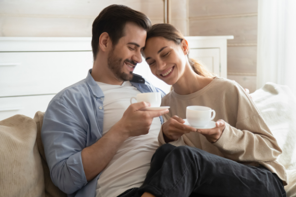 A man and a woman smiling while drinking tea on a couch together