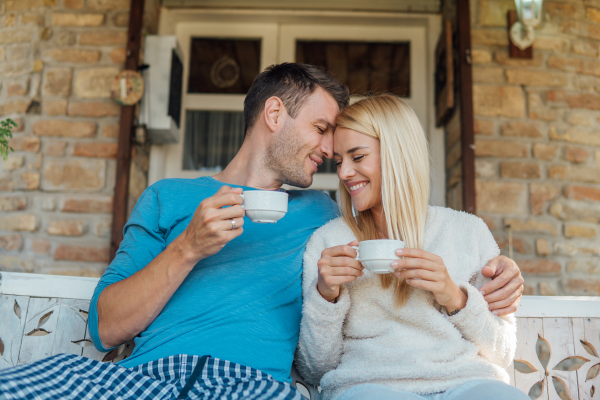 A man with his arm around a woman while drinking tea on a porch
