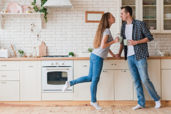 A man and a woman standing in a kitchen while drinking tea
